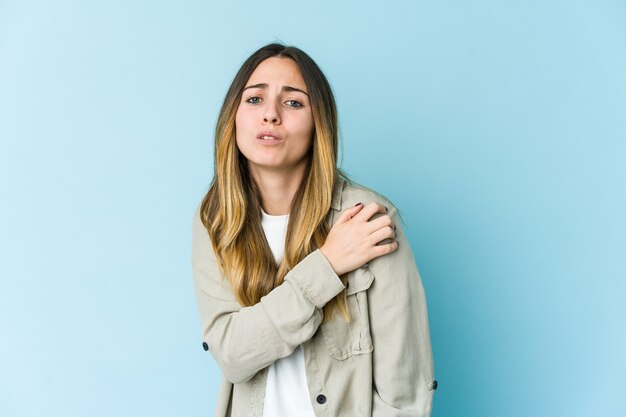 Young caucasian woman on blue having a shoulder pain.