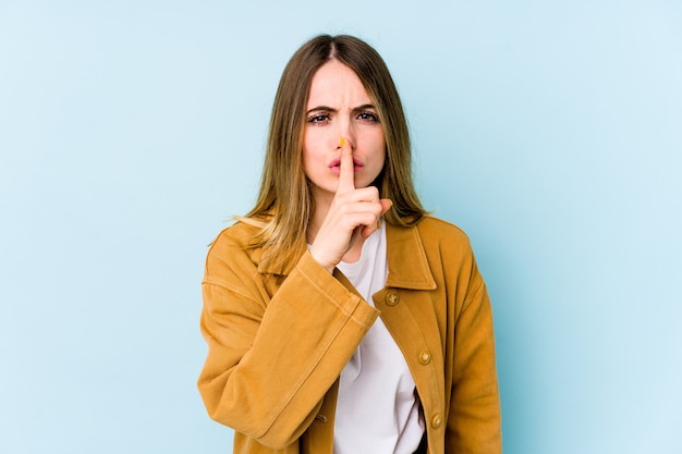 Young caucasian woman on blue keeping a secret or asking for silence.