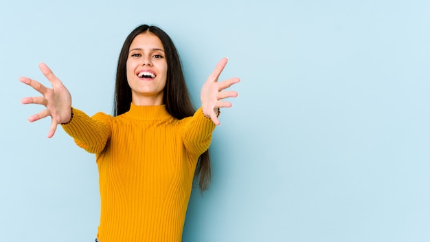 Young caucasian woman on blue wall feels confident giving a hug