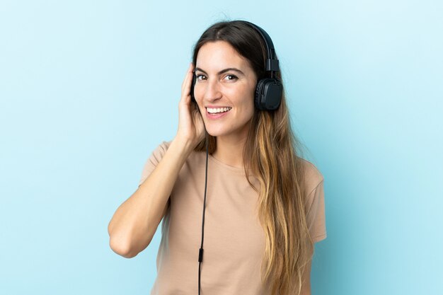 Young caucasian woman on blue wall listening music