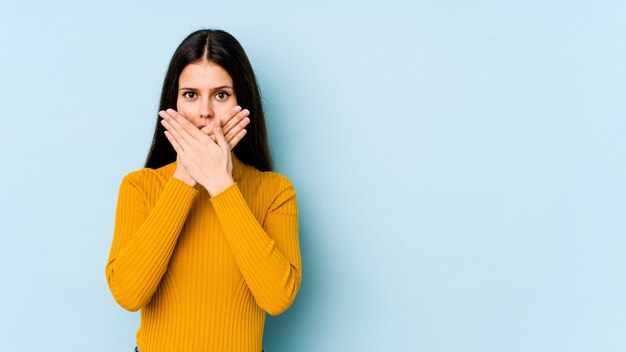 Young caucasian woman on blue wall shocked covering mouth with hands