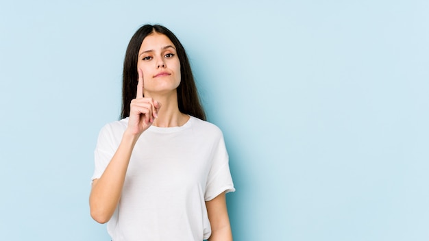 Giovane donna caucasica sulla parete blu che mostra il numero uno con il dito.