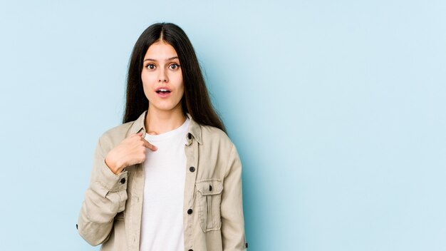 Young caucasian woman on blue wall surprised pointing with finger, smiling broadly.