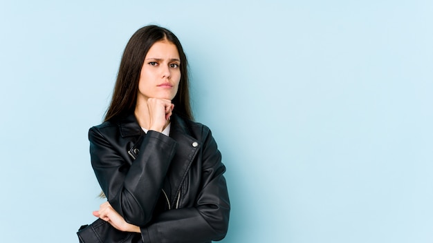 Young caucasian woman on blue wall suspicious