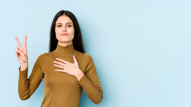 Giovane donna caucasica sulla parete blu facendo un giuramento, mettendo la mano sul petto.