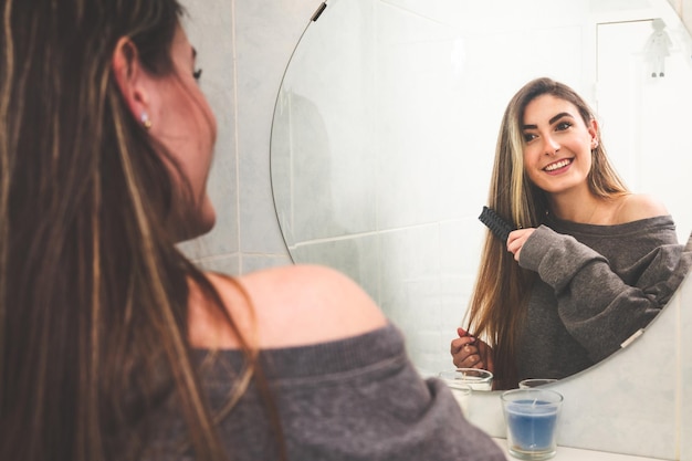 Young caucasian woman brushing her hair at mirror of a bathroom.