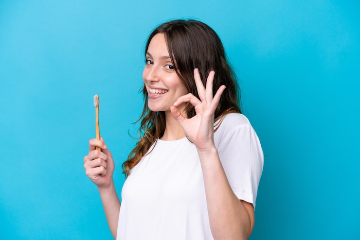 Photo young caucasian woman brushing teeth isolated on blue background showing ok sign with fingers