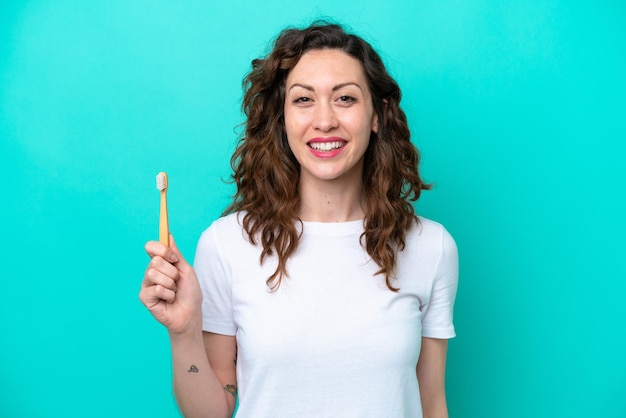 Young caucasian woman brushing teeth isolated on blue background smiling a lot