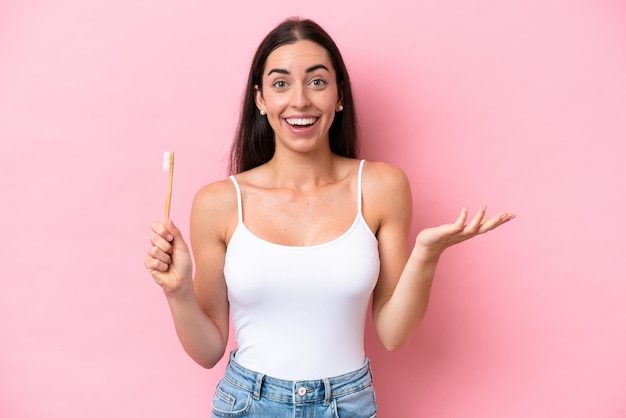 Young caucasian woman brushing teeth isolated on pink background with shocked facial expression