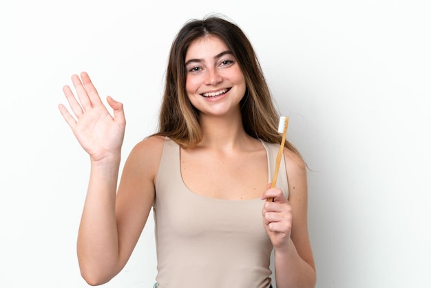 Young caucasian woman brushing teeth isolated on white background saluting with hand with happy expression