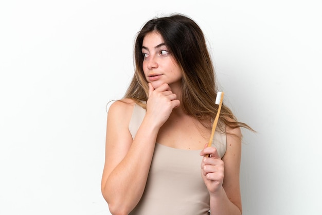 Young caucasian woman brushing teeth isolated on white background thinking an idea and looking side