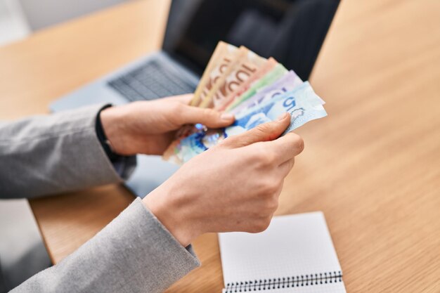 Young caucasian woman business worker using laptop counting canada dollars at office