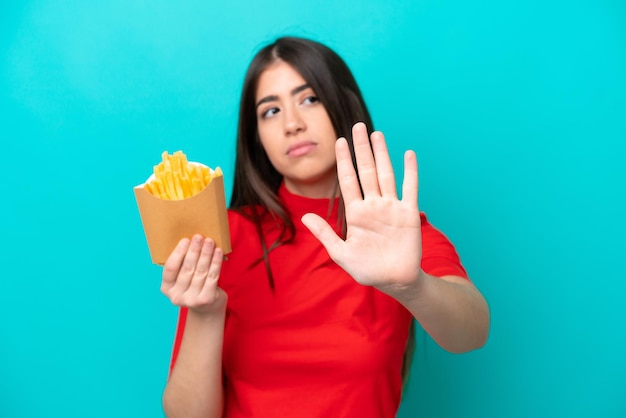 Young caucasian woman catching french fries isolated on blue\
background making stop gesture and disappointed