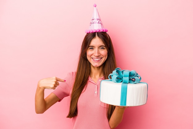 Giovane donna caucasica che celebra un compleanno isolato su sfondo rosa persona che indica a mano uno spazio copia camicia, orgogliosa e fiduciosa