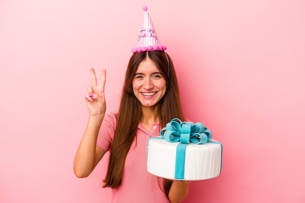 ピンクの背景に分離された誕生日を祝う若い白人女性は、指で2番目を示しています。