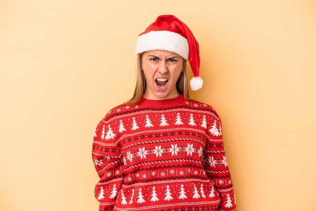 クリスマスを祝う若い白人女性は非常に怒って攻撃的に叫んで黄色の背景に分離されました。