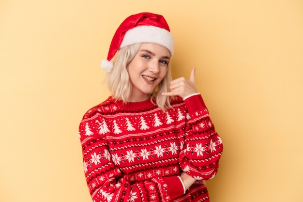 Young caucasian woman celebrating Christmas isolated on yellow background showing a mobile phone call gesture with fingers.