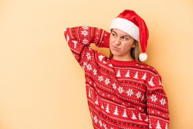 Young caucasian woman celebrating Christmas isolated on yellow background touching back of head, thinking and making a choice.