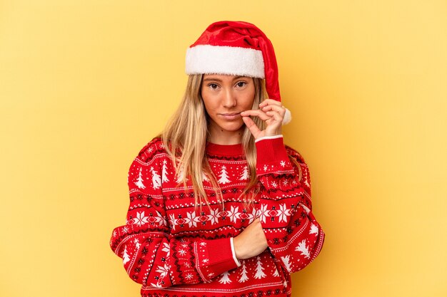 Young caucasian woman celebrating Christmas isolated on yellow background with fingers on lips keeping a secret.