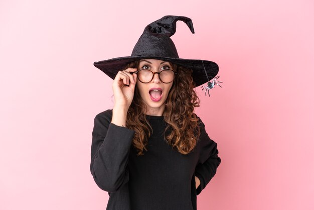 Young caucasian woman celebrating halloween isolated on pink background with glasses and surprised