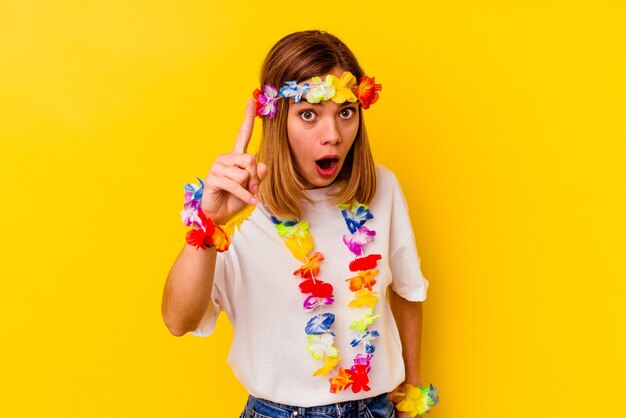 Young caucasian woman celebrating a hawaiian party isolated on yellow having an idea, inspiration concept