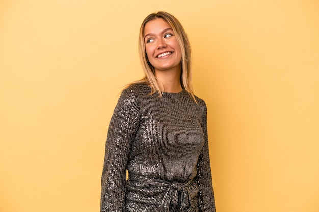 Young caucasian woman celebrating new year isolated on yellow background looks aside smiling, cheerful and pleasant.