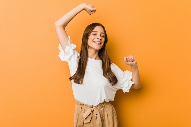 Young caucasian woman celebrating a special day, jumps and raise arms with energy