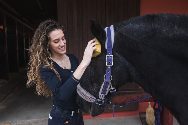 Giovane donna caucasica che pulisce e prepara un cavallo.