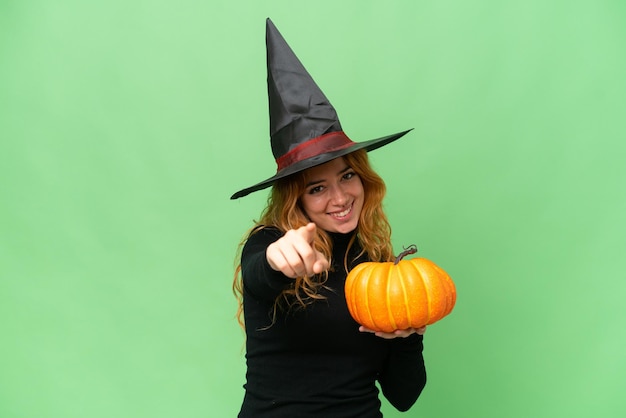 Young caucasian woman costume as witch holding a pumpkin isolated on green screen chroma key background pointing front with happy expression