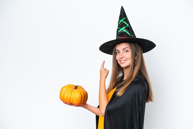 Costume da giovane donna caucasica come strega che tiene una zucca isolata su sfondo bianco che punta indietro