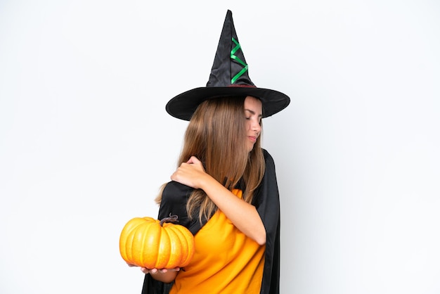 Young caucasian woman costume as witch holding a pumpkin isolated on white background suffering from pain in shoulder for having made an effort