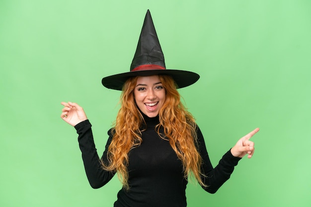 Young caucasian woman costume as witch isolated on green screen\
chroma key background pointing finger to the laterals and\
happy