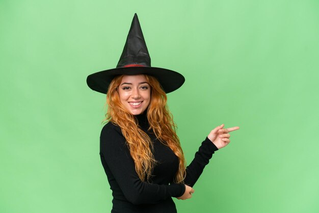 Foto costume da giovane donna caucasica come strega isolata sullo sfondo chiave cromatica dello schermo verde che punta il dito di lato