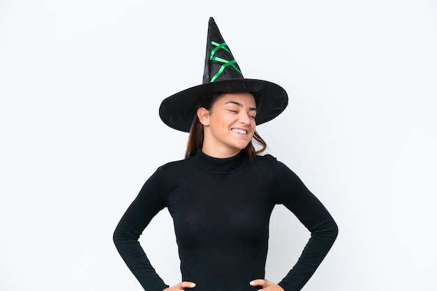 Young caucasian woman costume as witch isolated on white background posing with arms at hip and smiling