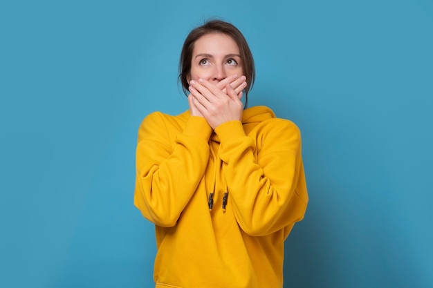 Young caucasian woman covering her mouth with hands Studio shot on blue wall