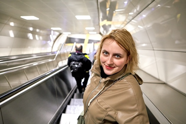 Young caucasian woman descends on an escalator to metro station.