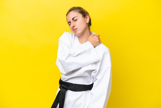 Young caucasian woman doing karate isolated on yellow background suffering from pain in shoulder for having made an effort