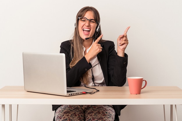 Giovane donna caucasica che fa telelavoro isolato su sfondo bianco che punta con l'indice a uno spazio di copia, esprimendo eccitazione e desiderio.