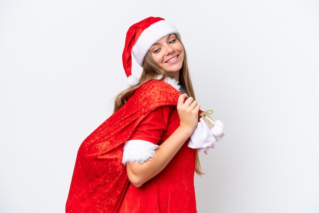 Молодая кавказская женщина, одетая как мама Ноэль, держит рождественский мешок на белом фоне со счастливым выражением лица