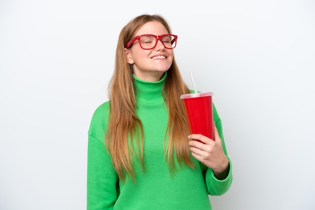 Young caucasian woman drinking soda isolated on white background laughing