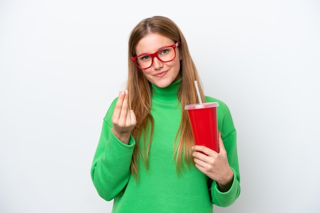 Young caucasian woman drinking soda isolated on white background making money gesture