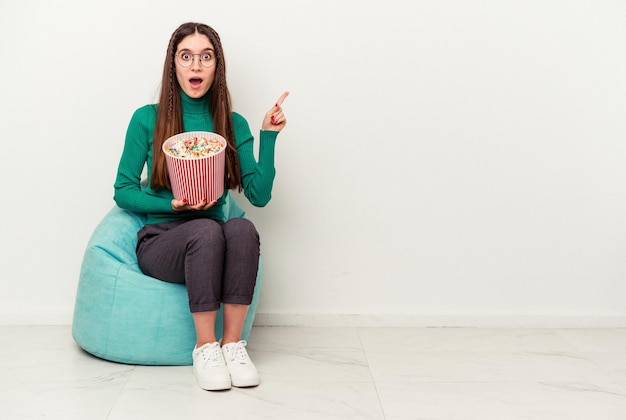 側面を指している白い背景で隔離のパフでポップコーンを食べる若い白人女性