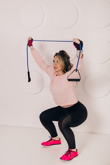 Photo young caucasian woman fitness instructor training in front of white wall with rubber resistance band