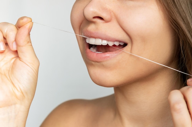 A young caucasian woman flossing her teeth after meal isolated on a gray background