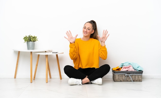 指で10を数える白い背景で隔離の床に座って服を折りたたむ若い白人女性