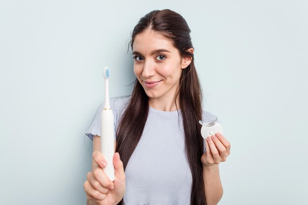 Young caucasian woman getting a dental whitening and electric
toothbrush isolated on blue background