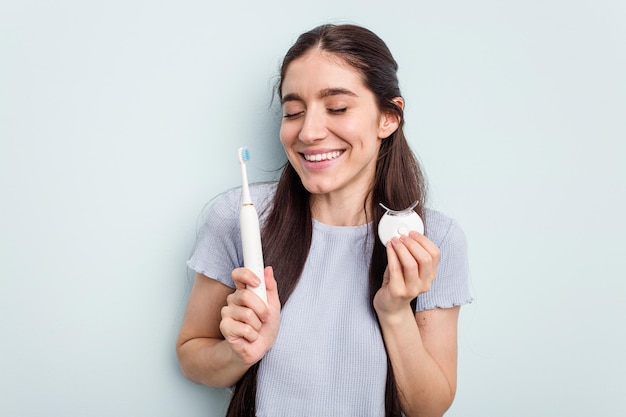 Young caucasian woman getting a dental whitening and electric\
toothbrush isolated on blue background