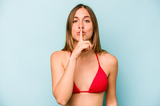 Young caucasian woman going to the beach isolated on blue background keeping a secret or asking for silence