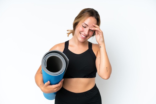 young caucasian woman going to yoga classes while holding a mat isolated on white background laughing