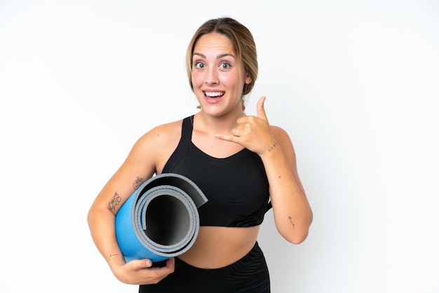 Young caucasian woman going to yoga classes while holding a mat isolated on white background making phone gesture Call me back sign